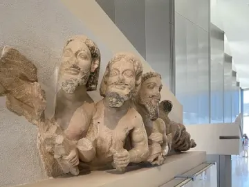 Trisomatos Typhon limestone figures displayed on a museum plinth, including a winged bearded torso.