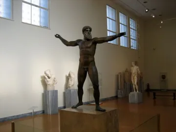 Artemision Bronze statue of a nude, bearded man with outstretched arms in a museum gallery.