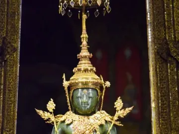 The Emerald Buddha seated on a golden pedestal beneath an ornate canopy with gilded columns and jeweled decorations.