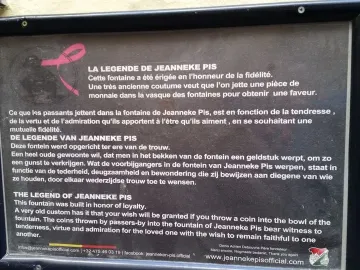 A rectangular sign about the legend of Jeanneke Pis mounted on a textured wall.