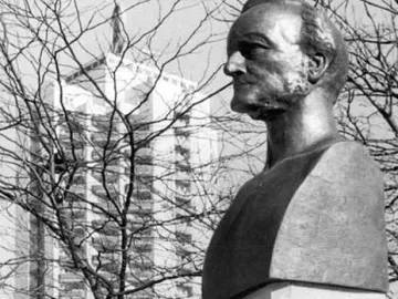Richard Wagner bust on a stone base with his name carved into it, with bare branches and a tall apartment building in the background.