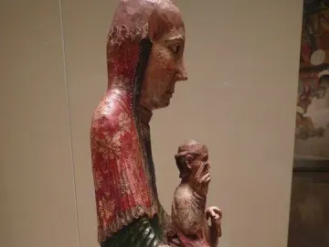 Virgin from Ger wooden carving shown in profile, with a robed figure holding a smaller figure on its lap.