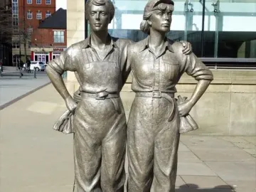 Women of Steel bronze sculpture of two women standing arm in arm in work clothes.