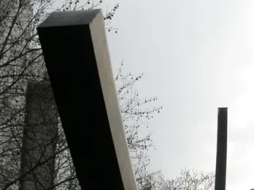 Bernar Venet’s Arc de 124,5° sculpture rising over a grassy area with bare trees and city buildings in the background.