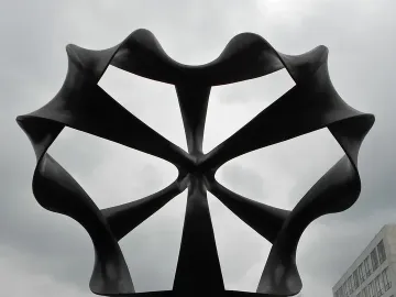 Continuum sculpture with dark, looping metal forms radiating from a central point against a cloudy sky.