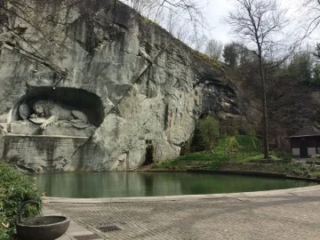 The Lion Monument in Lucerne carved into a rock face beside a reflective pond and paved walkway.