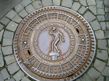 Koblenzer Schängel relief on a circular manhole cover in cobblestone pavement