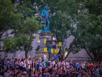 Albert Pike Memorial statue surrounded by a crowd holding candles and protest signs.