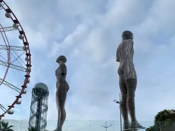Ali and Nino sculpture with two slatted human figures facing each other, with a ferris wheel and spiral tower in the background.
