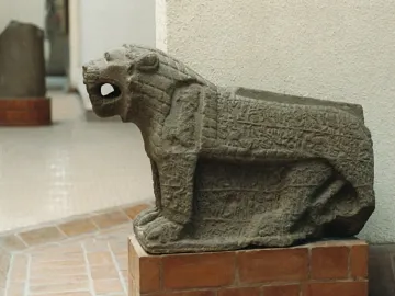 Maraş lion stone sculpture with an open mouth, carved in low relief and set on a brick pedestal.