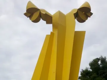 Ángel Custodio, a tall yellow abstract sculpture with wing-like forms at the top against a cloudy sky.