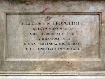 Weathered stone panel from the Canapone monument with an Italian inscription carved into a recessed section and colorful splatters on the surface.