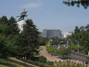 Chollima Statue of a winged horse with two figures on a tall pedestal, surrounded by trees and city buildings.