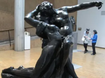 The Eternal Springtime bronze sculpture of a man embracing a woman, displayed on a pedestal in a museum gallery.