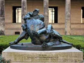 Bronze sculpture of Hercules grappling with the Nemean Lion on a stone pedestal outdoors.