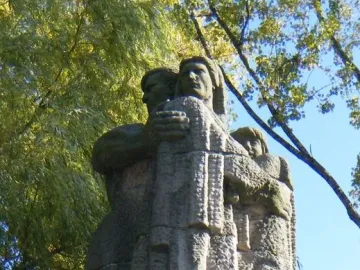 War Never Again stone monument showing a man embracing a woman and child on a tiered base inscribed “NIGDY WOJNY.”