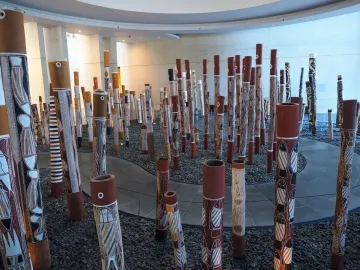 Aboriginal Memorial installation with numerous decorated cylindrical poles in a modern gallery space.