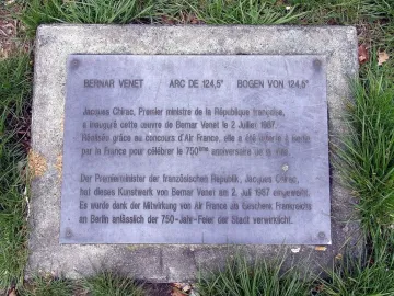 Metal plaque for Bernar Venet’s Arc de 124,5° set into a weathered concrete base in the grass.