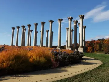 Capitol Columns standing above colorful autumn foliage with a curved path nearby under a blue sky.