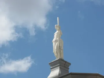 Girl with an Oar statue seen from below against a blue sky with clouds.