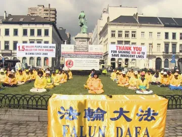 The John Cockerill Monument stands in a Brussels square with demonstrators gathered on the grass in front of it.