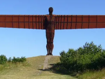 The Angel of the North sculpture stands on a grassy hill with outstretched wings under a clear blue sky.