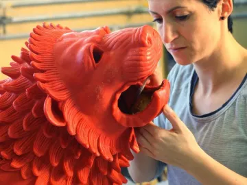 A woman works on the open mouth of the Chimera of Arezzo sculpture with a slender tool.