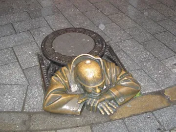 Čumil bronze sculpture of a man emerging from a manhole on a wet street