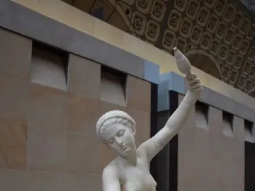 Jeune fille de Mégare, a white marble statue of a seated young woman spinning with a spindle and distaff.
