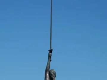 Verity sculpture seen from behind, holding a raised sword and scales against a blue sky.