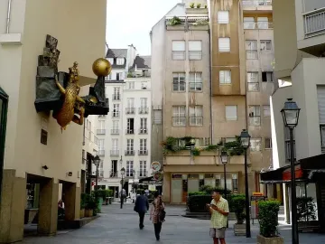 The Defender of Time clockwork sculpture on a building wall in Paris, showing a golden beast, a sphere, and a small sword-bearing figure.