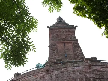 Kyffhäuser Monument seen from below, framed by green trees against a clear sky.