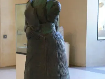 Napir-Asu statue seen from the back and right side, with a long draped garment and dark patinated surface.