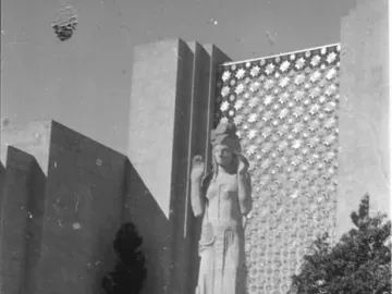 Pacifica statue stands before a geometric exhibition building with crowds gathered around the base.