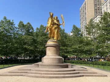 Sherman Monument with a golden equestrian statue on a stone base in a park setting.