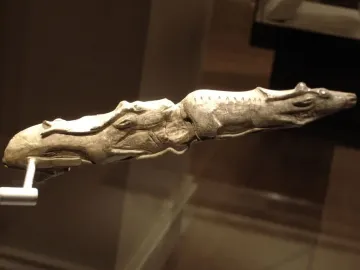 Elongated ivory carving of two swimming reindeer on a metal stand.