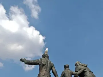 Auswandererdenkmal sculpture group on a tall granite pedestal, with a seagull perched on the central figure\'s head.