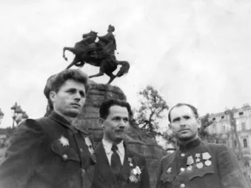 Upper portion of the Monument to Bohdan Khmelnytsky with a rider on a rearing horse above a rocky pedestal, partly obscured by three men in the foreground.