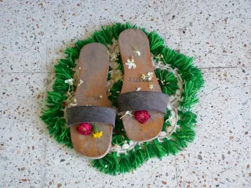 Charan Paduka sandals adorned with flowers on a green mat.