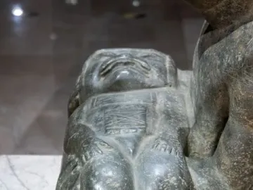 Close-up of the Las Limas Figurine showing a squat carved figure with a broad face and detailed chest designs, held by part of a larger figure.