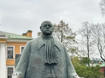 Peter I Monument showing a bronze seated figure in a long coat and cravat among low bushes.
