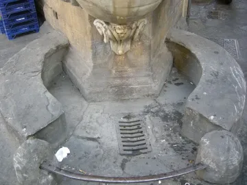 Lower section of Fontana dello Sprone with a grotesque face spouting water into a circular marble basin.