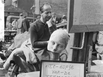 Detached head of The Little Mermaid resting on a metal pitcher beside a framed sign reading \