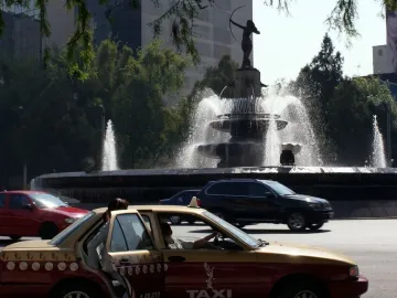 Diana the Huntress Fountain rises above city traffic, with a red and yellow taxi in the foreground.