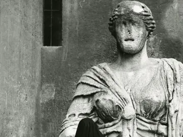 Madama Lucrezia, a weathered stone statue of a woman, stands on a pedestal beside a dark-robed figure seen from behind.
