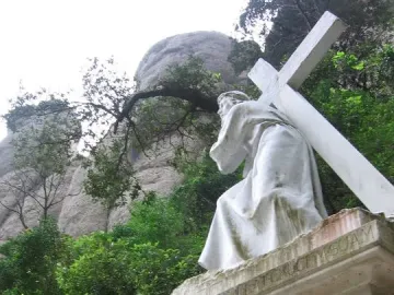 Monumental Rosary of Montserrat statue of a robed figure carrying a large cross on a pedestal.