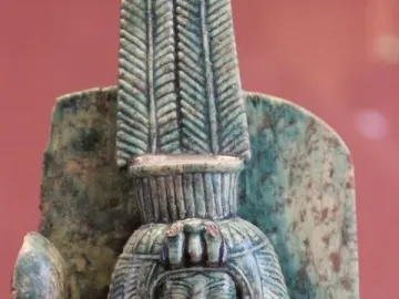 Bust of Queen Tiye with a tall segmented headdress and broad wig, holding an arched object.