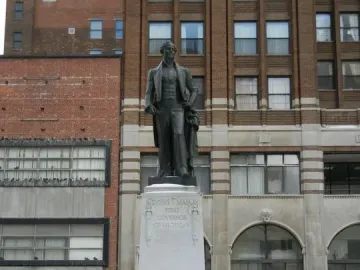 Stevens T. Mason Monument on a snowy stone pedestal beside downtown buildings.