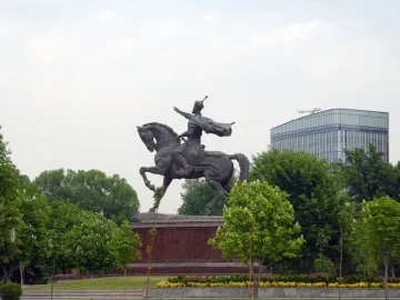 Timur equestrian statue on a reddish-brown pedestal surrounded by trees and flowers.