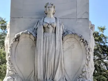 A classical female figure on the Alamo Cenotaph holds shields above inscribed panels.